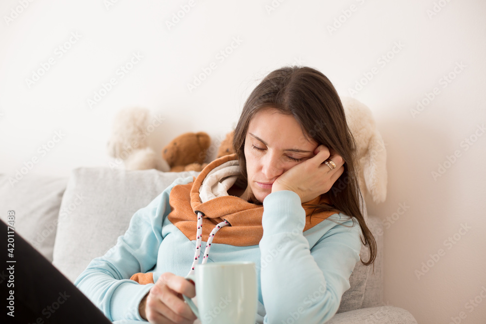 Tired mother, sitting on the couch with a cup of coffee after sleepless night Tired mother, sitting on the couch with a cup of coffee after sleepless night