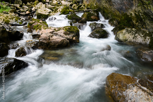 Beautiful long exposure photo of rapids and small waterfalls between big moss covered rocks.