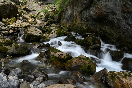 Beautiful photo of rapids and small waterfalls between big moss covered rocks.