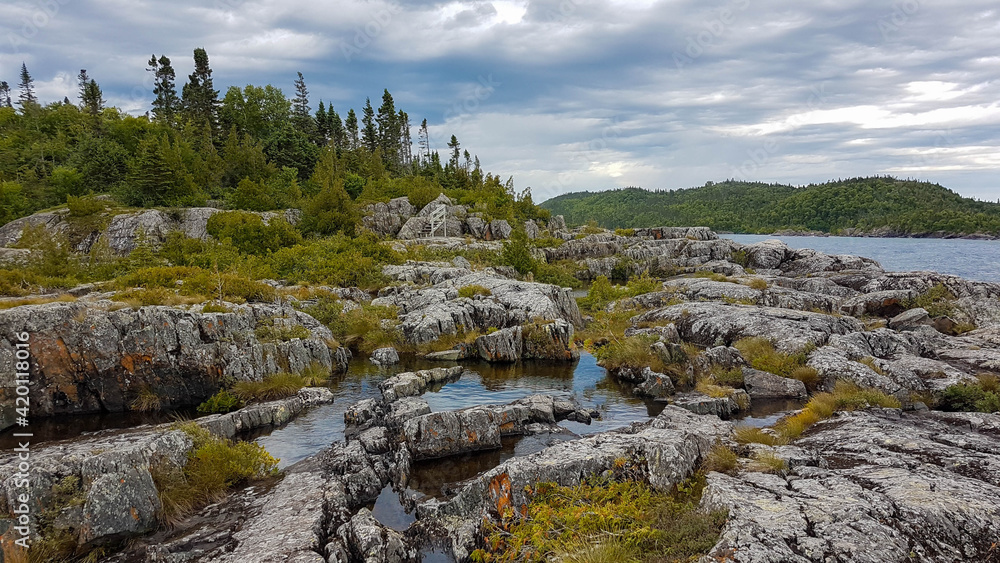 Senic landscape of the Lake Superior coastline in the Pukaskwa Nationalpark. A rocky hillside covered with bushes and ponds next to a mixed forest.