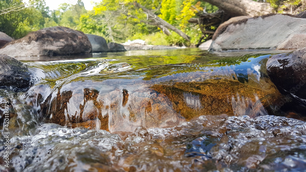 Closeup of a stone bathed by a creek creating a scenic little transparent waterfall.