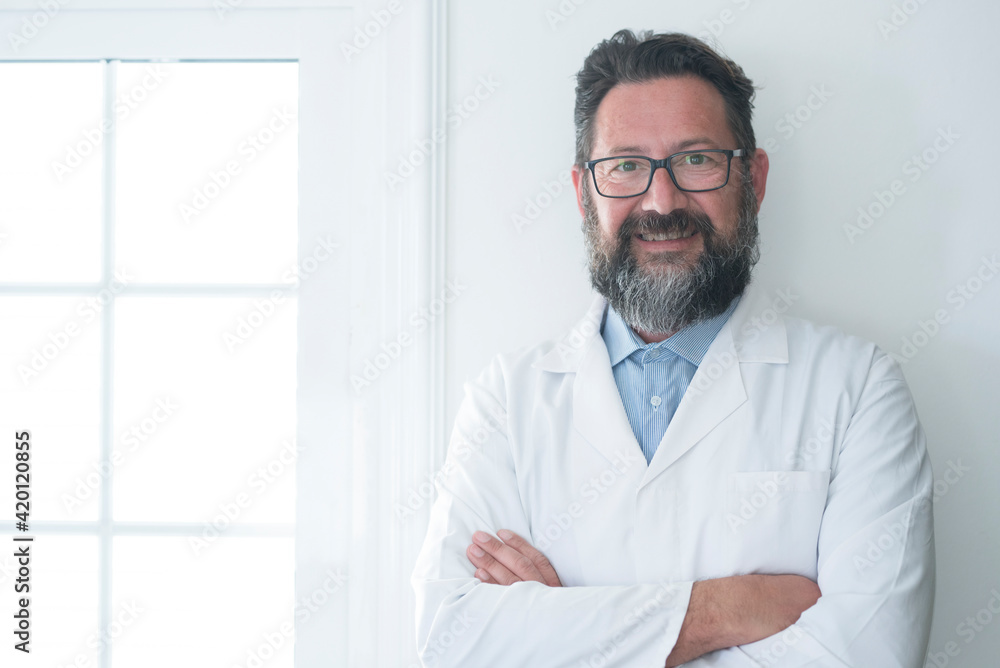 Cheerful mature doctor posing and smiling at camera, healthcare and medicine - adult cheerful man with hospital look standing and looking - health visit concept at doc studio office Cheerful mature doctor posing and smiling at camera, healthcare and medicine - adult cheerful man with hospital look standing and looking - health visit concept at doc studio office