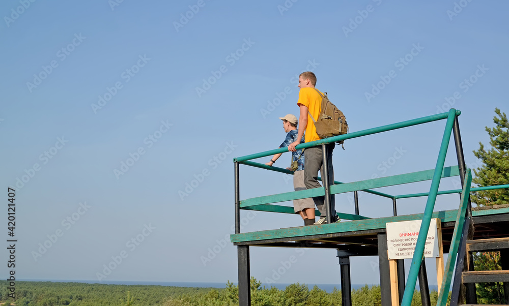 Two young tourists stand on the observation deck on the Curonian Spit. Russian text - no more than 12 people on the observation deck