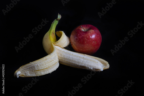 Opened colorful banana and red apple isolated on black