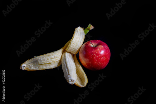Opened colorful banana and red apple isolated on black