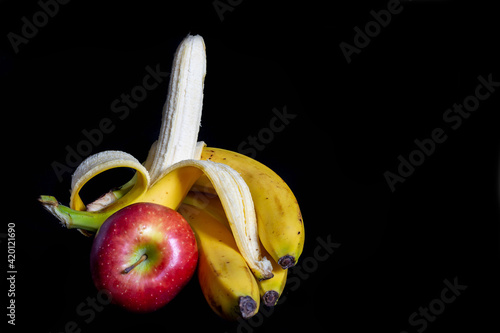 Opened colorful banana and red apple isolated on black