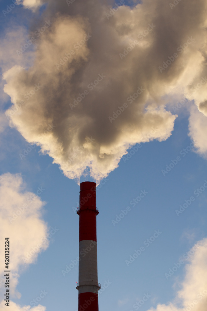 Huge clouds of steam from the pipes and boilers of the city Thermal Power Plant against the blue sky.
