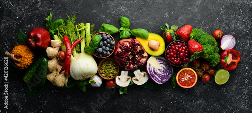 Fresh vegetables and fruits: fennel, avocado, pomegranate, berries, cabbage and basil. Organic healthy vegan food. On a black stone background.
