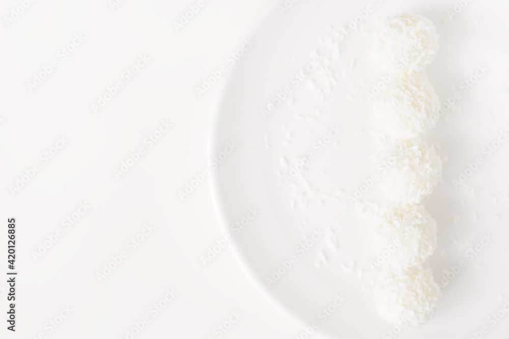 Food photography of natural vegetarian raw food candies with coconut. Close-up white round coconut candy on a white, delicate and airy background. Empty space for text. Flat lay top-down. Food photography of natural vegetarian raw food candies with coconut. Close-up white round coconut candy on a white, delicate and airy background. Empty space for text. Flat lay top-down.