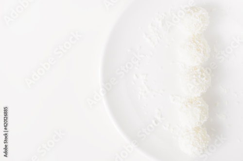 Food photography of natural vegetarian raw food candies with coconut. Close-up white round coconut candy on a white, delicate and airy background. Empty space for text. Flat lay top-down.