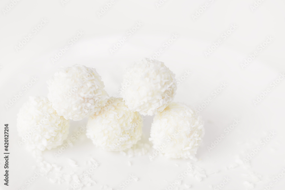 Food photography of natural vegetarian raw food candies with coconut. Close-up white round coconut candy on a white, delicate and airy background. Empty space for text. Flat lay top-down.
