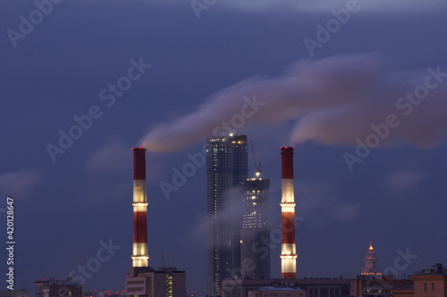 Cityscape overlooking the chimneys of the thermal power station with white clouds of steam in cold winter day.