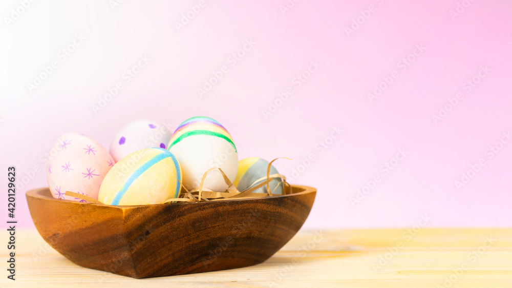 Fototapeta premium Colorful easter eggs on a wooden plate on a table on a pink background
