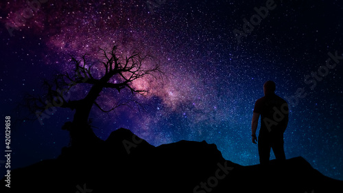 single dead tree and man silhouette at night with milky way core and stars background