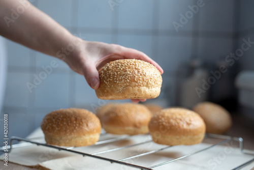 Female hand holding sesame seed hamburger bun in the kitchen, cooking at home.