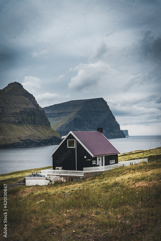 Black house on famous faroese Witches Finger Trail and Koltur island on background. Sandavagur village, Vagar island, Faroe islands, Denmark. Landscape photography Black house on famous faroese Witches Finger Trail and Koltur island on background. Sandavagur village, Vagar island, Faroe islands, Denmark. Landscape photography