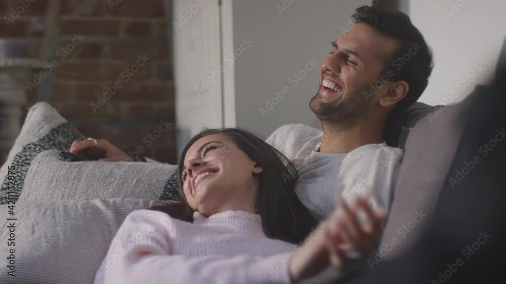 Evening shot of couple lying and relaxing on lounge sofa at home and watching TV together - shot in slow motion Evening shot of couple lying and relaxing on lounge sofa at home and watching TV together - shot in slow motion