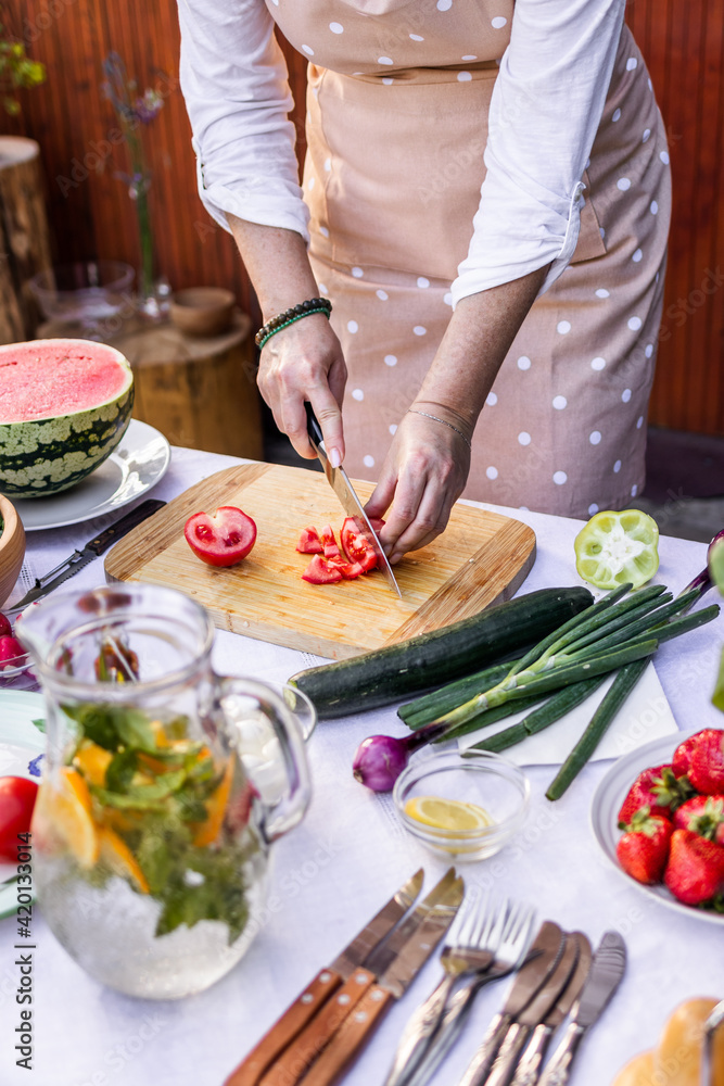Preparing vegetable salad outdoors. Woman chopping red tomato on cutting board