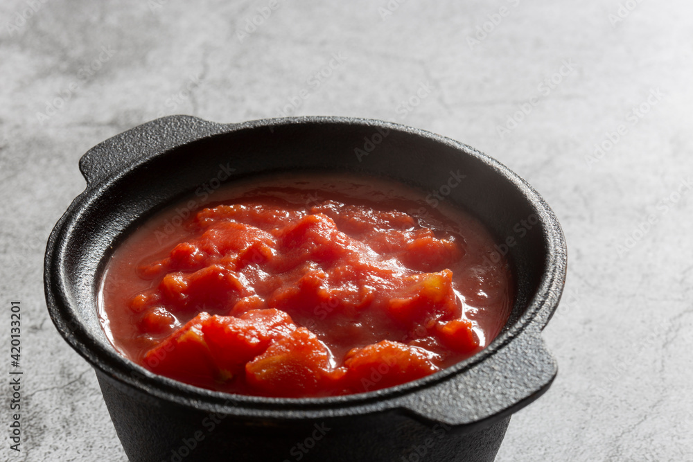 Chopped tomatoes cooked in a cast iron pot. On a concrete background Chopped tomatoes cooked in a cast iron pot. On a concrete background