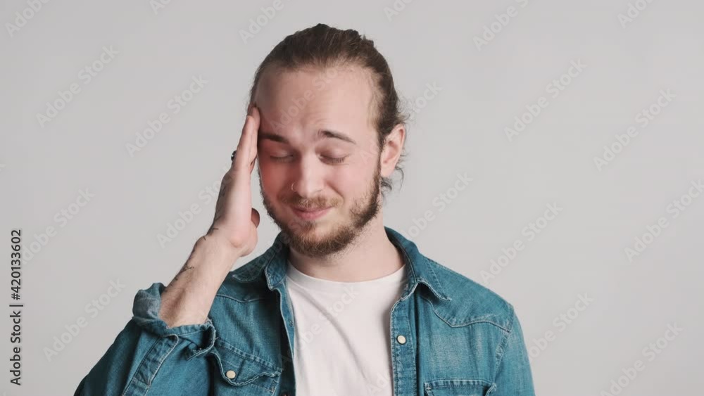 Young bearded man dressed in casual wear massaging temples feeling headache after hard day isolated on white background. Pain in head Young bearded man dressed in casual wear massaging temples feeling headache after hard day isolated on white background. Pain in head