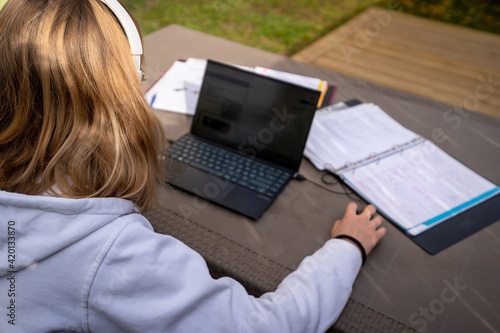 Une étudiante de dos travaille sur sa terrasse avec un ordinateur et un casque sur les oreilles