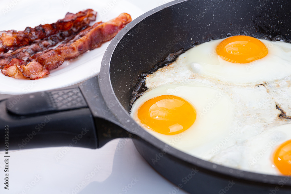 Fried eggs and bacon cooking in a skillet or pan. Idea for morning breakfast. Yellow yolks of eggs and red fried slices of bacon. Fried eggs and bacon cooking in a skillet or pan. Idea for morning breakfast. Yellow yolks of eggs and red fried slices of bacon.