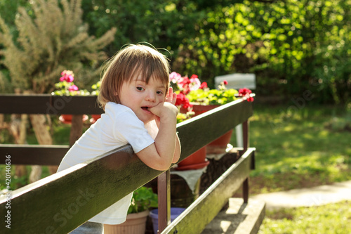Portrait of cute little boy with Down syndrome leaned on fence looking bored during quarantine..