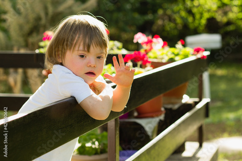 Baby boy with Down syndorme waving his hand on patio terrace outdoors at spring. Greets guests. Home leisure activity at quarantine.