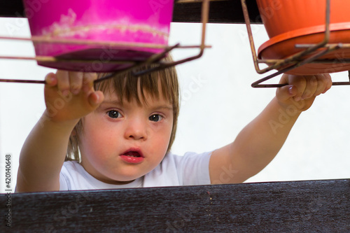 Portrait of little toddler, boy with down syndrome looking at camera while holding holders for flowerpot.