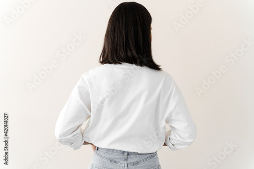 Millennial female wearing white t-shirt standing turning back to camera. Young woman standing isolated on white background in studio. Copyspace, corporate branding concept. photo