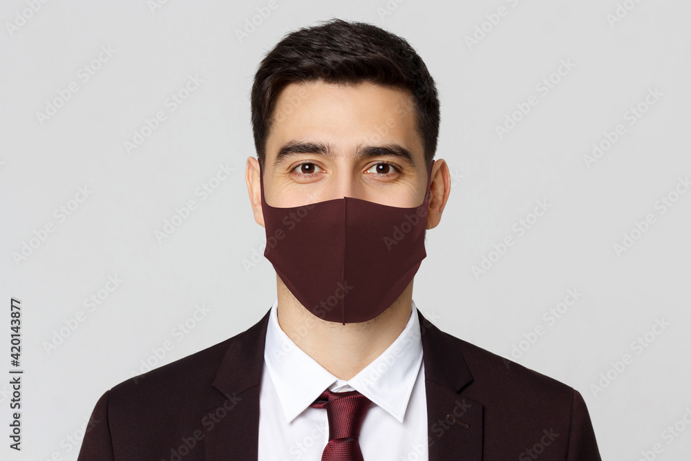 Portrait of smiling businessman wering maroon mask, standing against gray background Portrait of smiling businessman wering maroon mask, standing against gray background