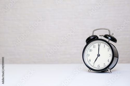 An alarm clock showing 7 o'clock standing on a white table with copy space, everyday shedule and morning wake up concept