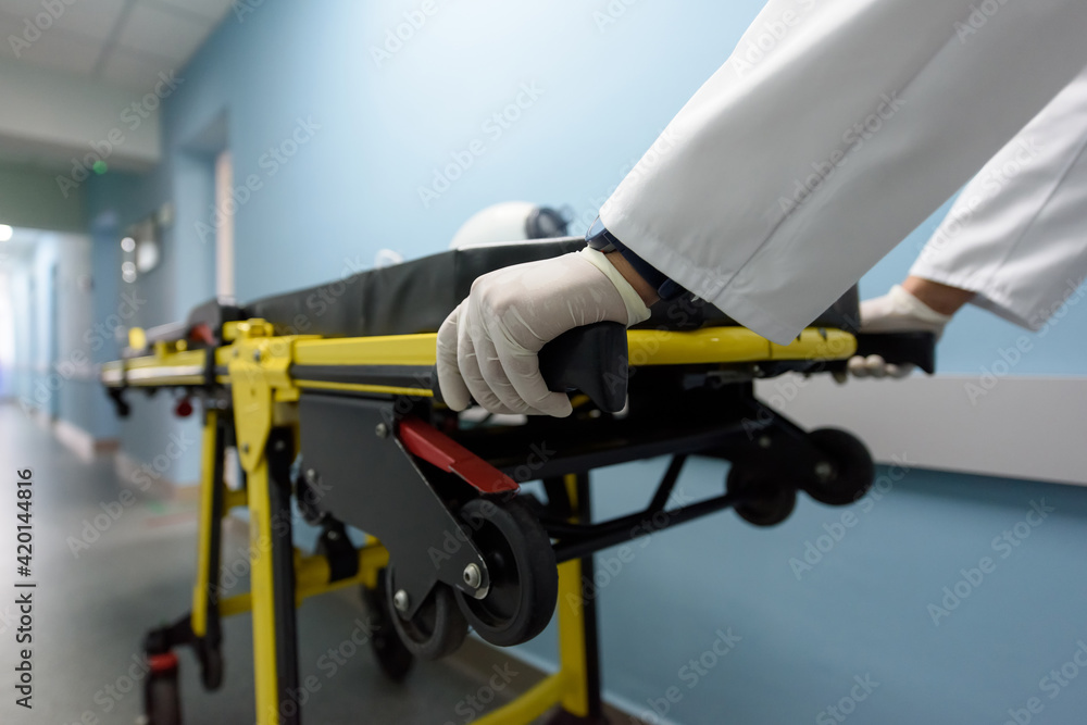 Emergency department in a modern hospital. A doctor or paramedic pushes a yellow ambulance stretcher down the corridor of the intensive care unit. Close-up shot, selective focus on the medic hands 
