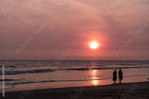 Kobiety spacerujące brzegiem oceanu o zachodzie słońca, ciemno pomarańczowy nastrojowy krajobraz. © insomniafoto