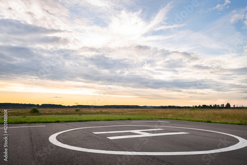 View of the private helipad on a warm summer evening. An asphalt helipad against the backdrop of a green field and a cloudy evening sky.