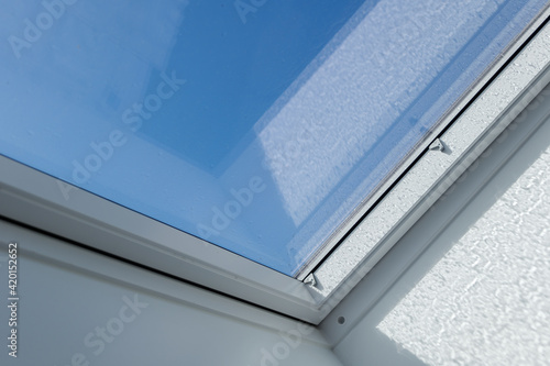 Close up view at white window Skylights with raindrop on glass at attic and background of sunny blue sky.