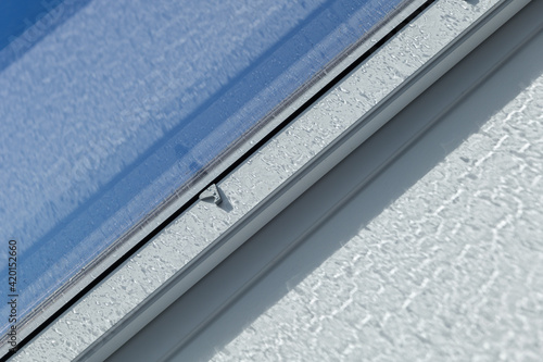 Close up view at white window Skylights with raindrop on glass at attic and background of sunny blue sky.