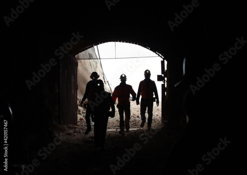 silhouettes of men with headlamps walking into mine