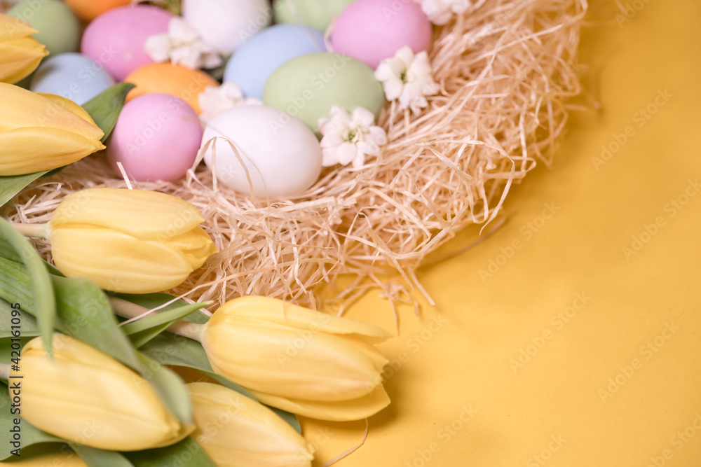 multicolored easter eggs on hay and near yellow tulips on yellow background multicolored easter eggs on hay and near yellow tulips on yellow background