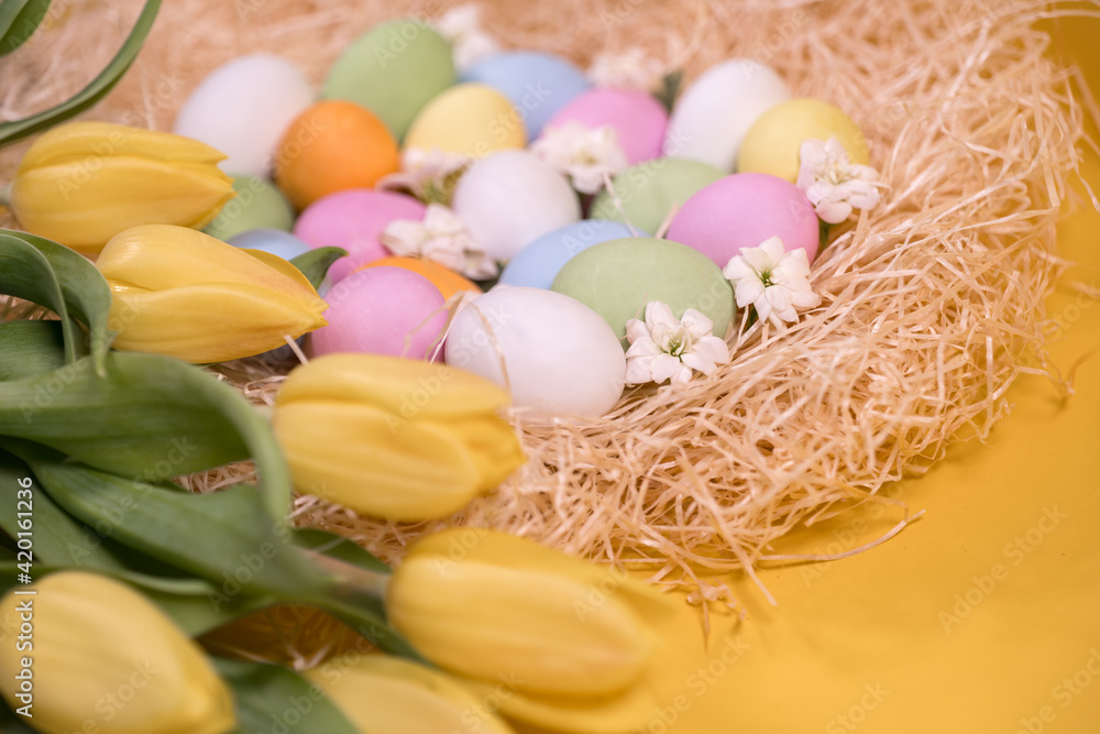 multicolored easter eggs on hay and near yellow tulips on yellow background
