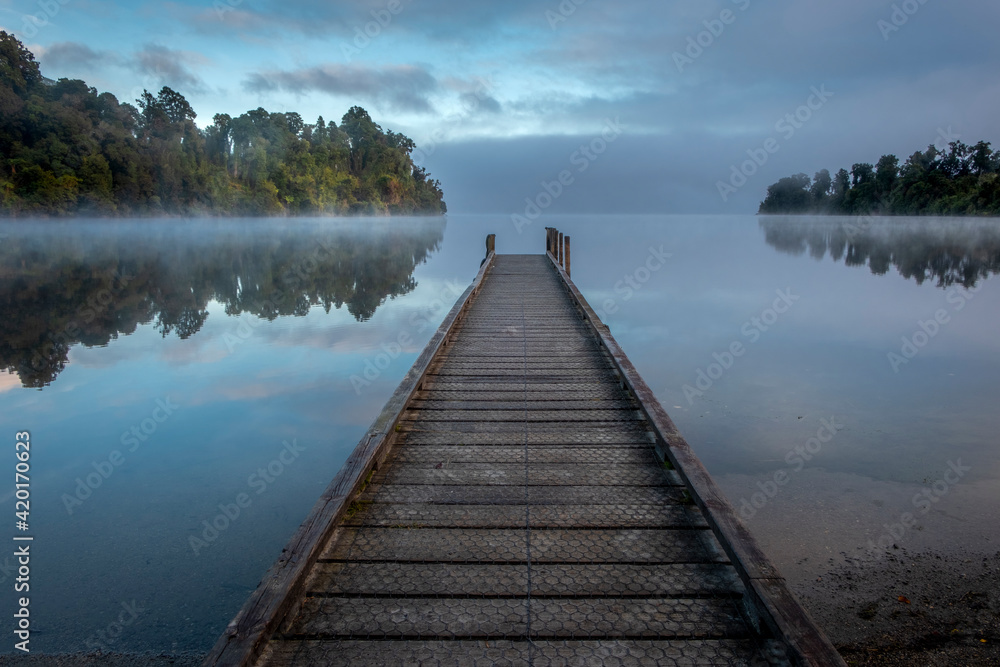Forest lake with little jetty on a misty morning. South Island, New Zealand.
