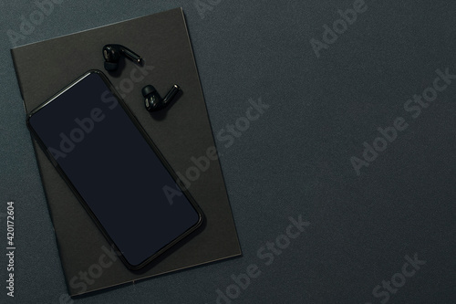 Blank screen smartphone and earphone on black cover book.