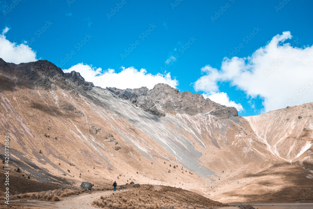 Fototapeta premium Adult man in the distance admiring the rocky landscape of the mountains partially covered with snow in the middle of a sunny day and with blue sky