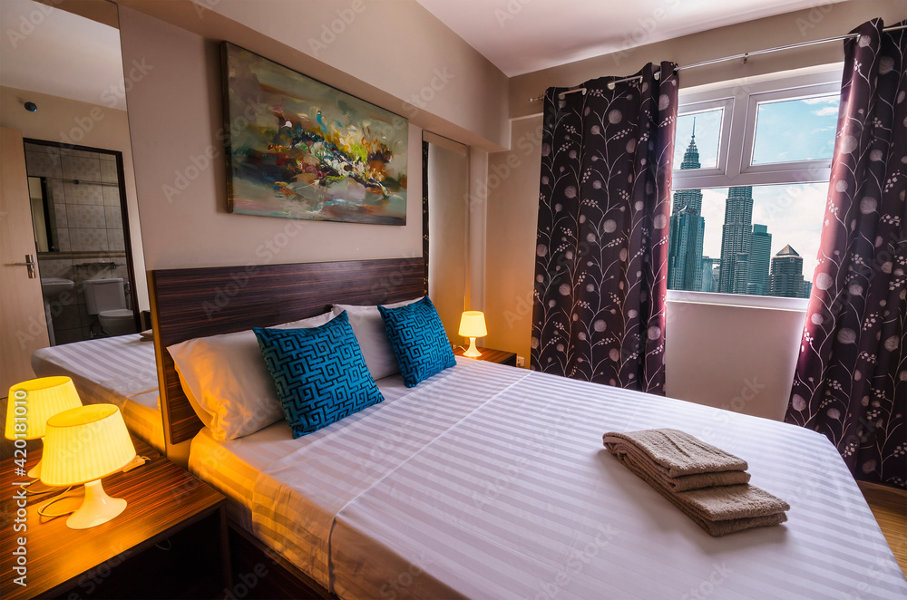 Fototapeta premium Kuala Lumpur, Malaysia - Feb 2020: Interior of the bedroom of a condominium or hotel with views of Petronas towers and the city skyline.