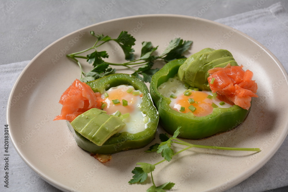 Fried eggs in green bell peppers with avocado and salmon on white plate Fried eggs in green bell peppers with avocado and salmon on white plate