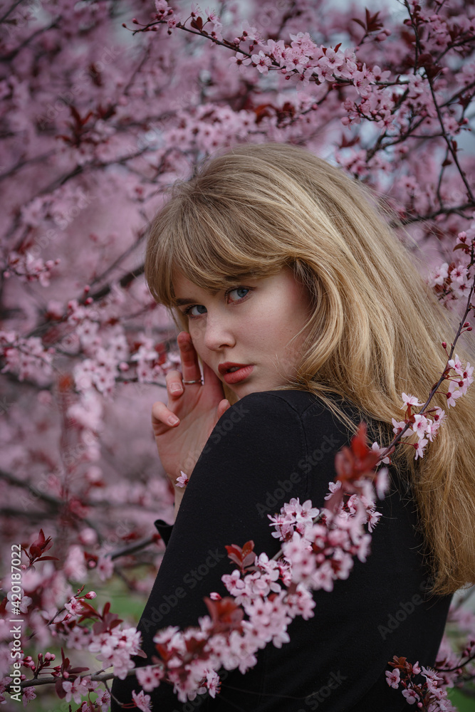 Fototapeta premium Outdoor fashion photo of a beautiful young lady in a pink cherry blossom garden