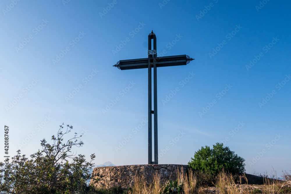 Iron cross on the mountain of El Rabat, in Valencia (Spain), La Safor region, on a day with blue skies, and surrounded by vegetation and flowers. Iron cross on the mountain of El Rabat, in Valencia (Spain), La Safor region, on a day with blue skies, and surrounded by vegetation and flowers.