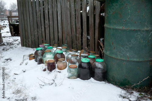 Old jars of pickles stand in the snow near an old fence on the street photo