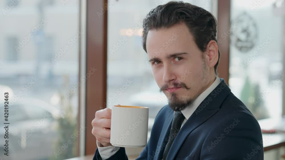 Close-up portrait of positive successful man clinking tea cup with camera and smiling. Happy relaxed Caucasian businessman drinking hot drink in cafe or restaurant. Joy and lifestyle. Close-up portrait of positive successful man clinking tea cup with camera and smiling. Happy relaxed Caucasian businessman drinking hot drink in cafe or restaurant. Joy and lifestyle.