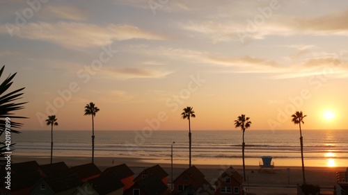 Palms silhouette sunset sky, California aesthetic. Oceanside USA. Tropical pacific ocean beach atmosphere. Los Angeles vibes. Lifeguard watchtower, palmtree and baywatch tower hut. Beachfront cottages